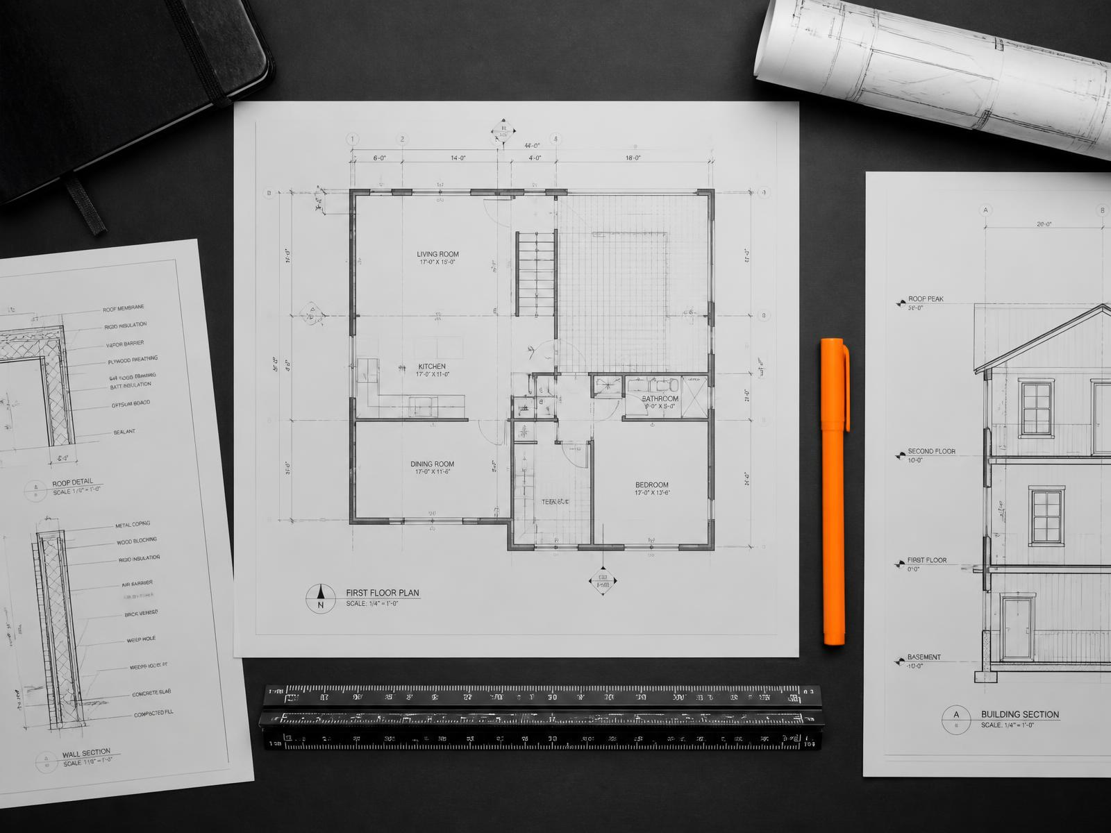 Architectural drawings, sections and a scale rule laid out on a dark surface